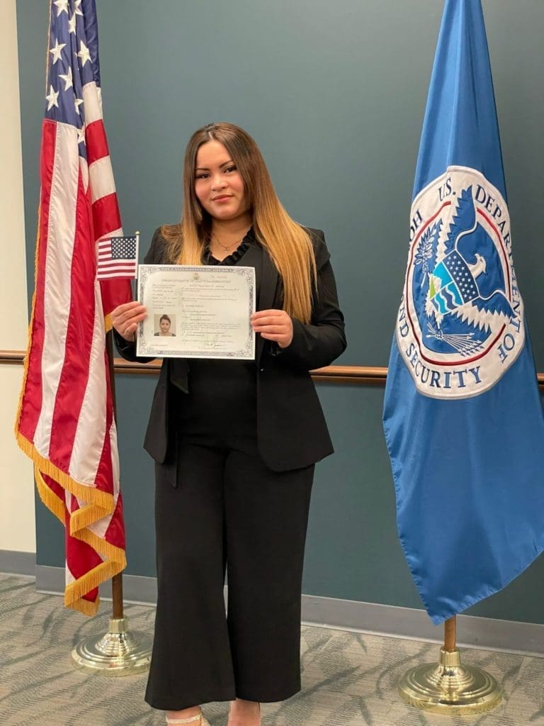 Latina young woman with bright smile holding up certificate for her naturalization ceremony