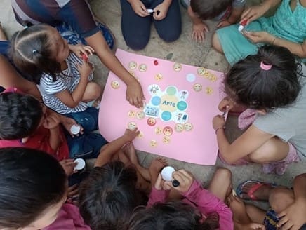 A group of children sitting down as they put emoji stickers on a pink poster 