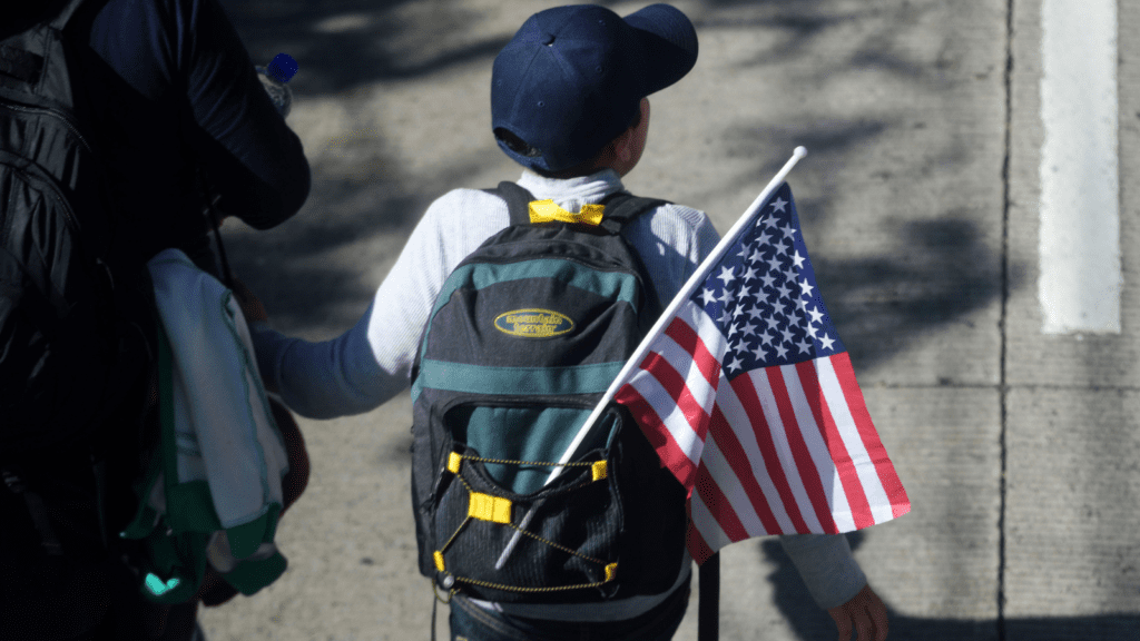 A young boy with a baseball cap and backpack with a U.S. flag on it embarks on a journey to seek safety and protection