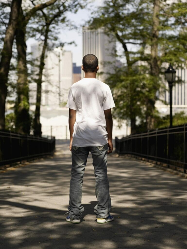 Teenage boy standing in park in front of buildings.