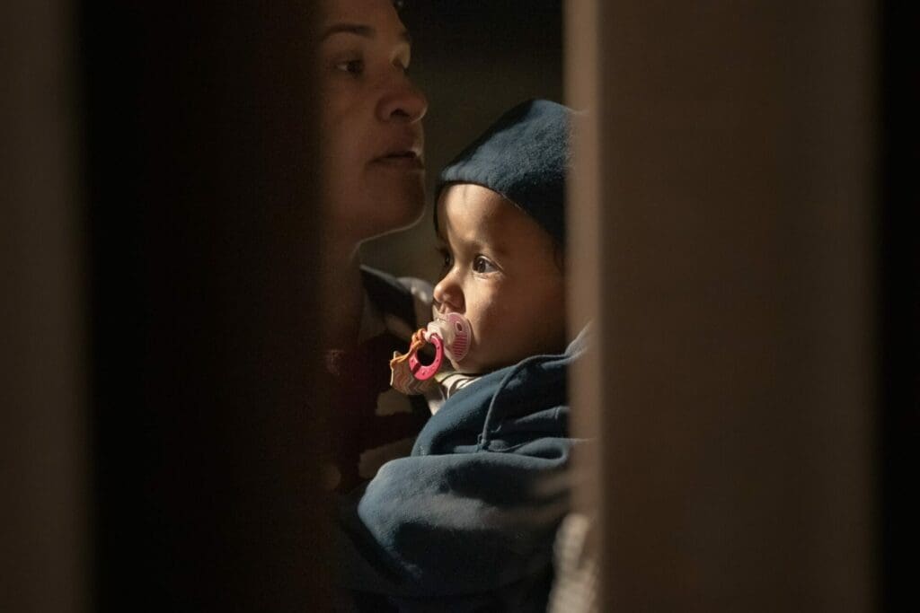 Mother holding child as they wait present themselves at the U.S.-Mexico border.