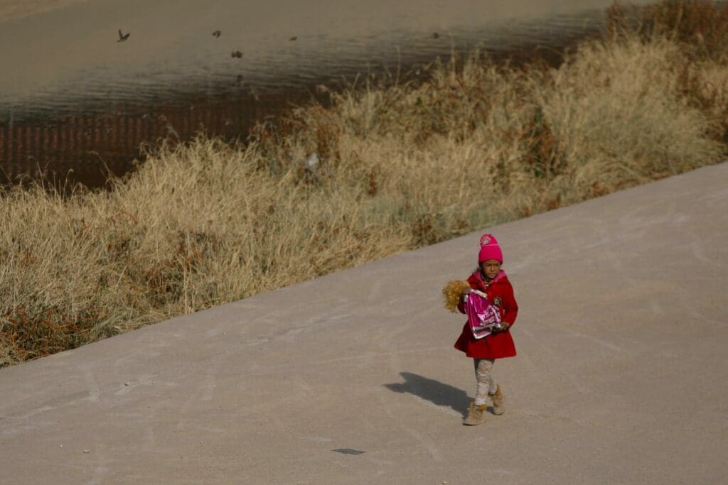 A Venezuelan migrant girl holds a doll while walking on the banks of the Rio Grande in Ciudad Juarez