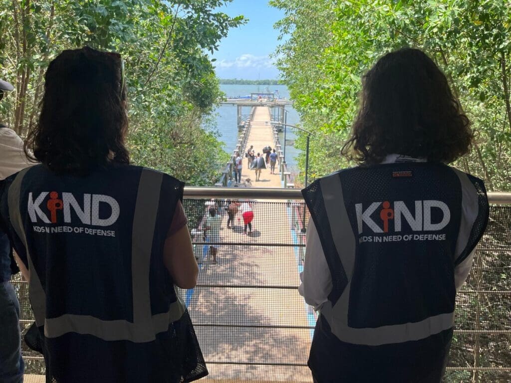 Two KIND staff members, standing on the bridge in Colombia as families board a boat to enter the Darien Gap.
